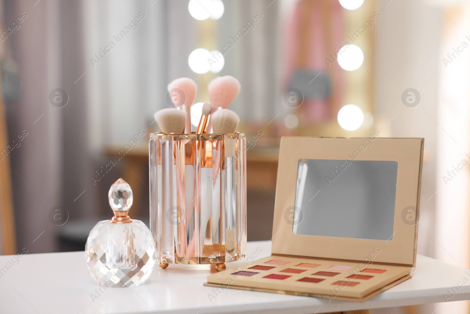 Photo of Set of brushes, eyeshadow palette and perfume on white table in makeup room