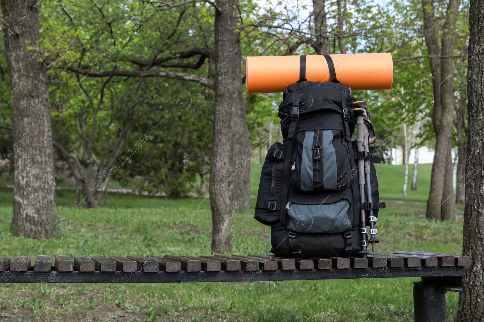 Photo of Backpack with camping mat and trekking poles on wooden bench in park. Space for text