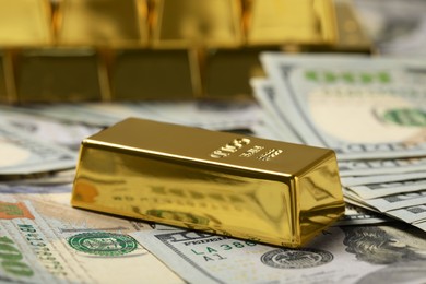 Photo of Shiny gold bar on dollar banknotes, closeup