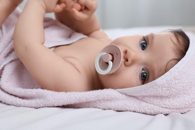 Photo of Cute little baby with pacifier in hooded towel after bathing on bed, closeup