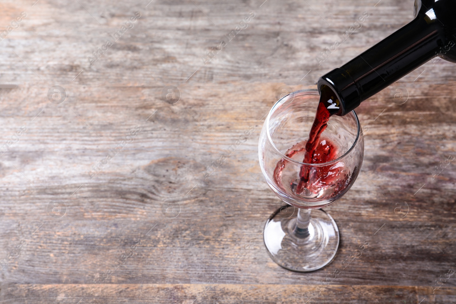 Photo of Pouring delicious red wine into glass on wooden background