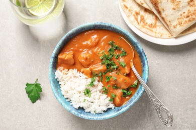 Photo of Delicious butter chicken with rice in bowl served on grey table, top view