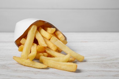 Photo of Paper box with delicious french fries on white wooden table, closeup. Space for text