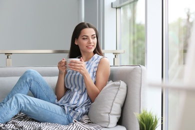 Photo of Young beautiful woman drinking morning coffee near window at home