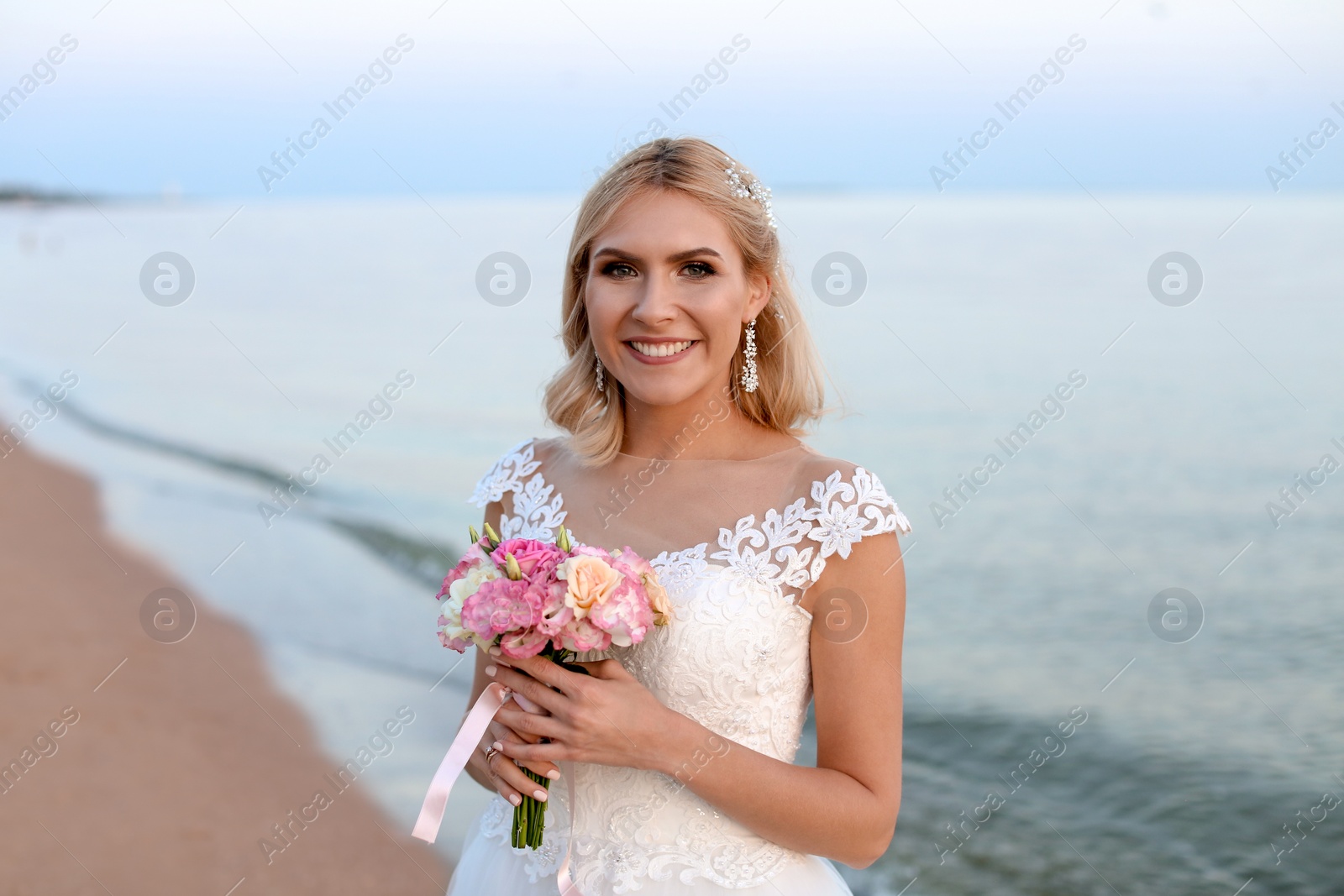 Photo of Happy bride holding wedding bouquet on beach