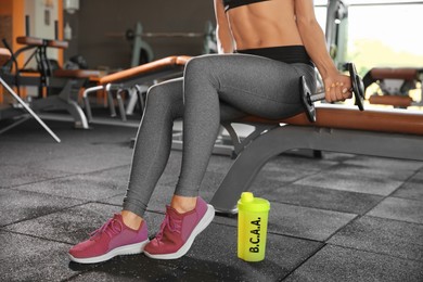 Image of Athletic woman and shaker with amino acids (BCAA) drink in gym, closeup