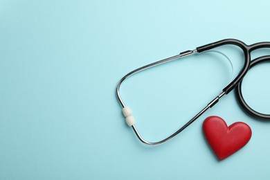 Photo of Stethoscope and red heart on light blue background, top view. Space for text