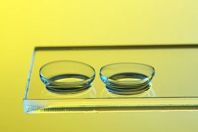 Pair of contact lenses on glass against pale yellow background, closeup