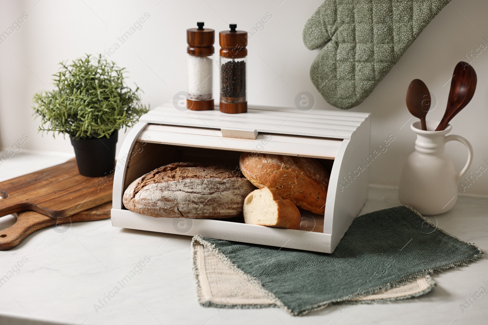 Photo of Wooden bread basket with freshly baked loaves on white marble table in kitchen