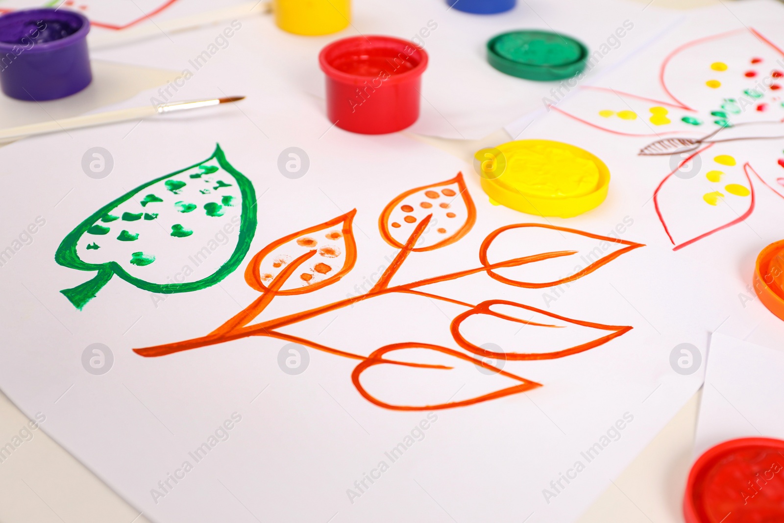 Photo of Cute children's drawing, brush and set of paints on white table, closeup