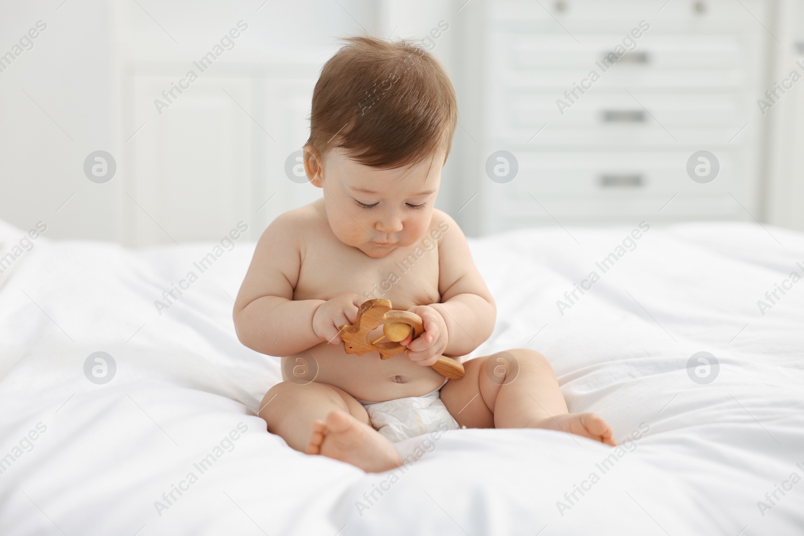 Photo of Cute baby boy with wooden rattle on bed at home