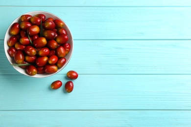 Palm oil fruits in bowl on turquoise wooden table, flat lay. Space for text