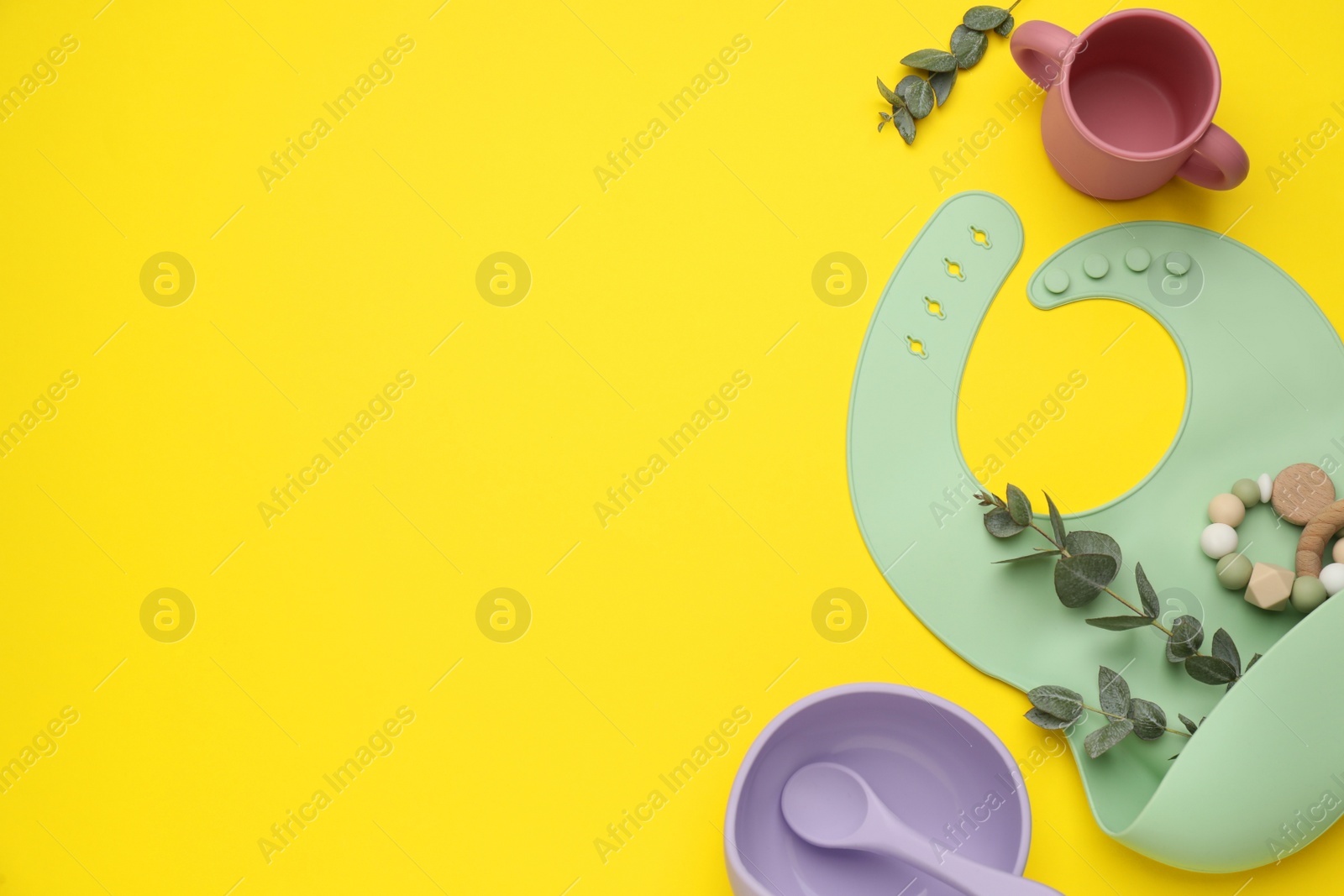 Photo of Set of plastic dishware and silicone bib on yellow background, flat lay with space for text. Serving baby food