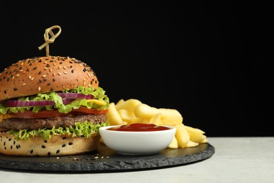 Photo of Burger with delicious patty, french fries and sauce on gray table against black background, space for text