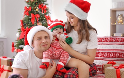 Happy couple with baby in Christmas hats at home
