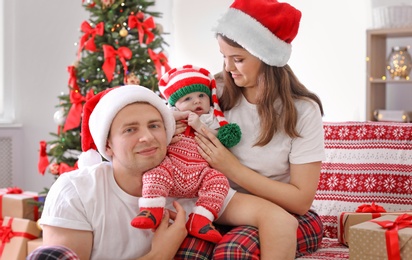 Photo of Happy couple with baby in Christmas hats at home