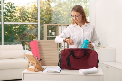 Businesswoman packing sports stuff for training into bag in office