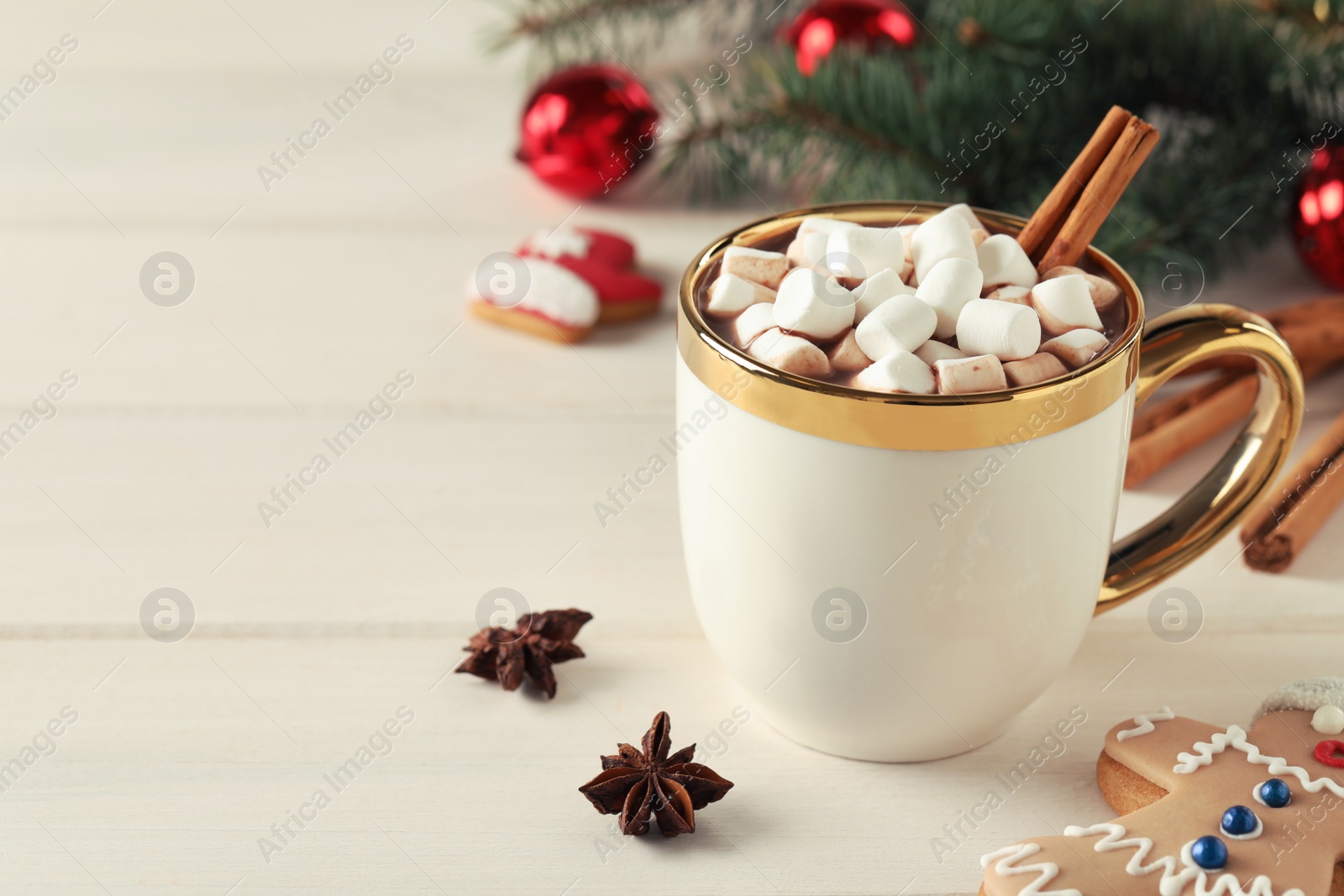 Photo of Delicious hot chocolate with marshmallows and cinnamon near Christmas cookie on white wooden table, space for text