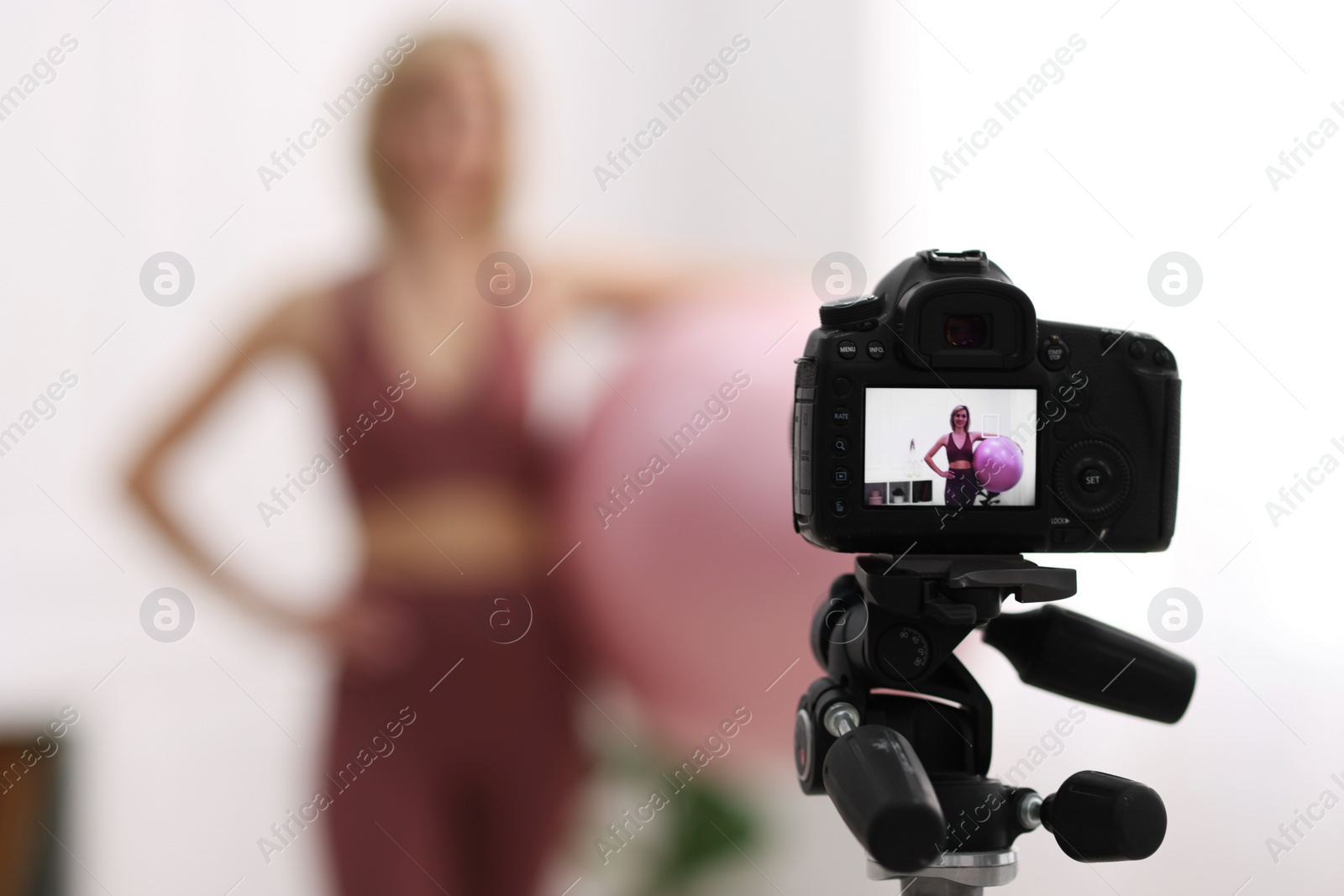 Photo of Smiling sports blogger with fit ball recording fitness lesson at home, focus on camera. Space for text