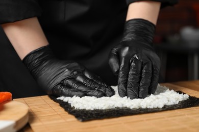Chef in gloves making sushi roll at table, closeup