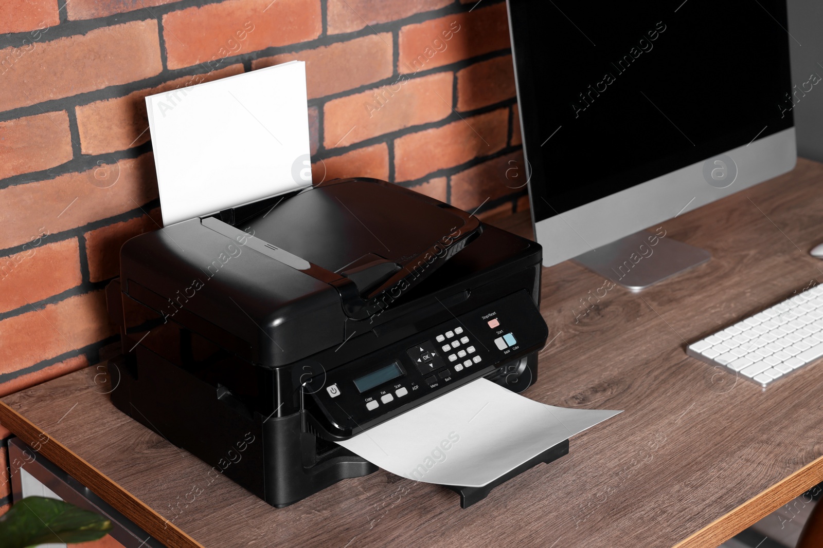 Photo of Modern printer with paper near computer on wooden desk at home