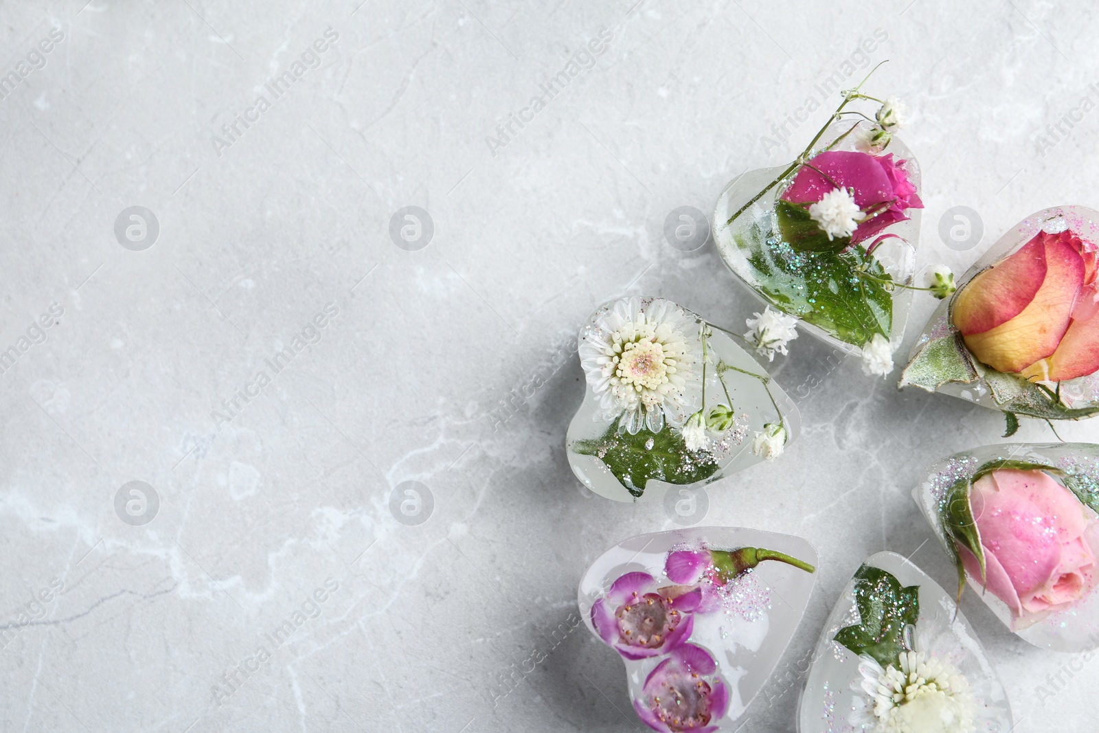 Photo of Heart shaped ice cubes with flowers on grey background, flat lay. Space for text