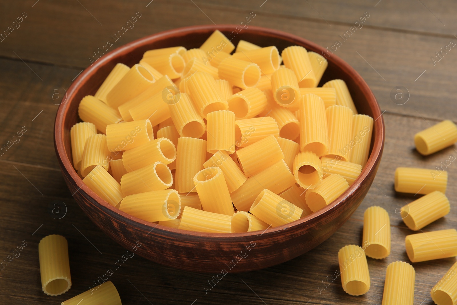 Photo of Raw rigatoni pasta in bowl on wooden table, closeup