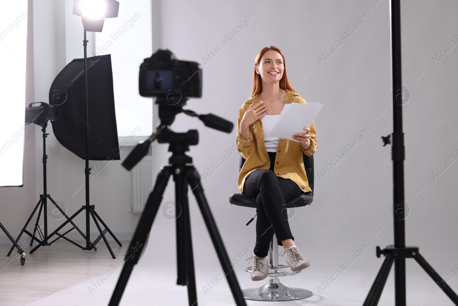 Photo of Casting call. Woman with script performing in front of camera against light grey background at studio