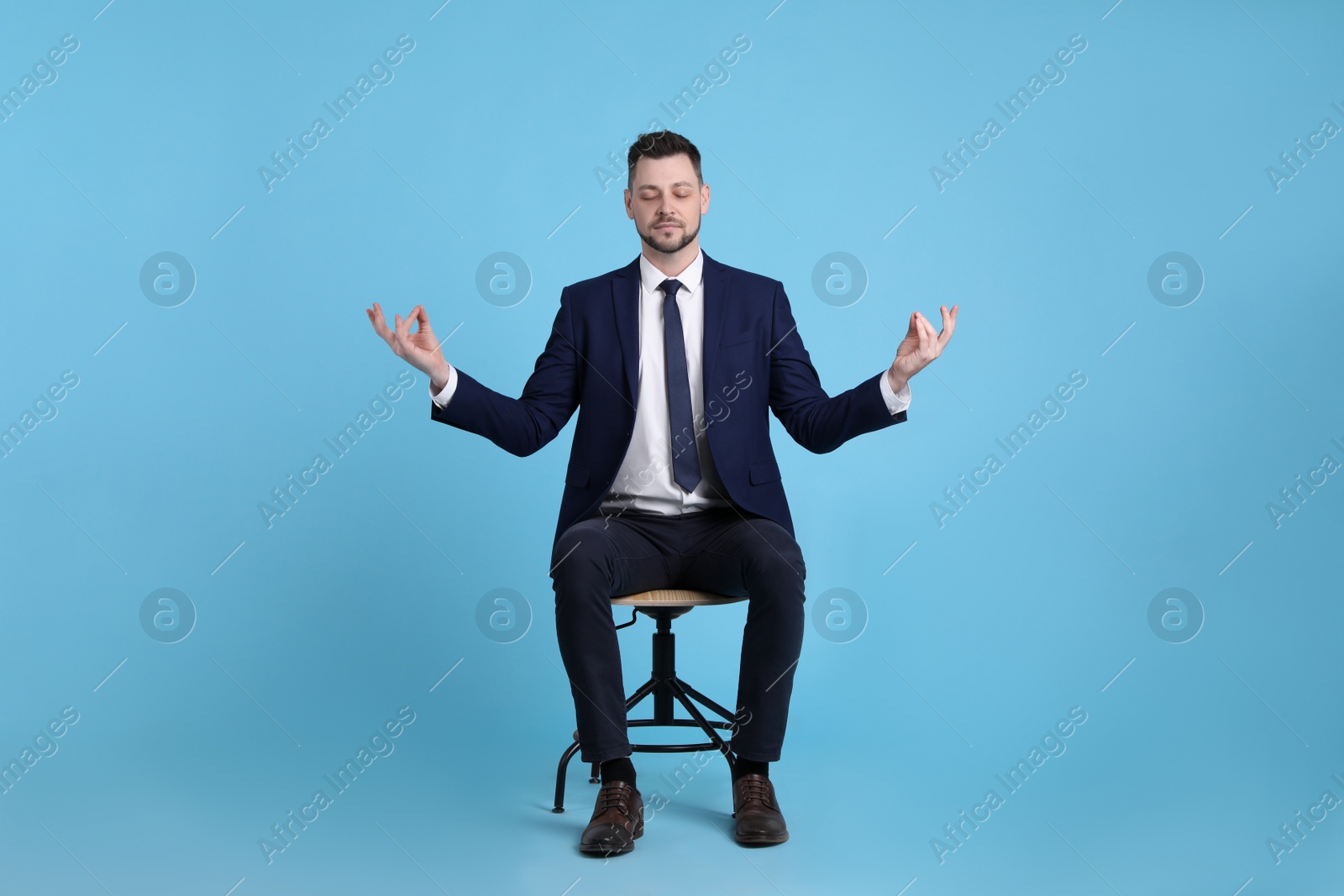 Photo of Handsome businessman meditating in office chair on light blue background