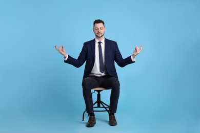 Handsome businessman meditating in office chair on light blue background