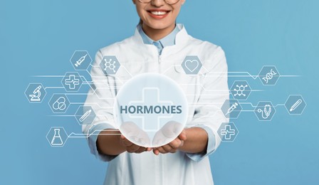 Doctor showing digital icons on light blue background, closeup. Hormones Balance