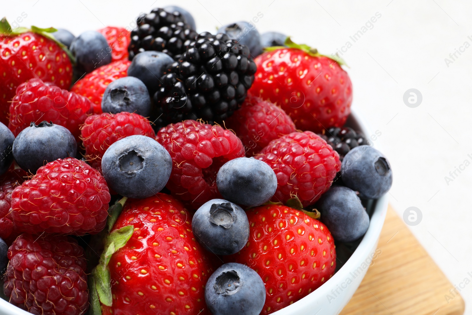 Photo of Many different fresh ripe berries in bowl on light grey table, closeup