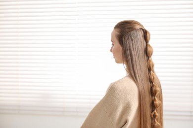 Photo of Young woman with long braided hair indoors, space for text