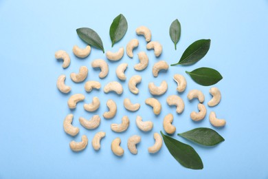 Photo of Many tasty cashew nuts and leaves on light blue background, flat lay