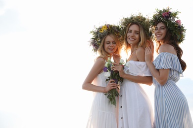 Young women wearing wreaths made of beautiful flowers outdoors on sunny day