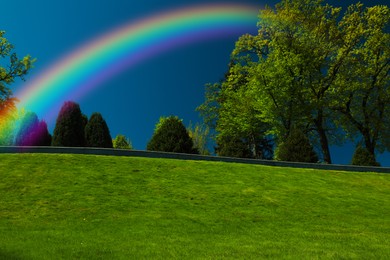 Image of Picturesque view of green meadow and beautiful rainbow in blue sky on sunny day