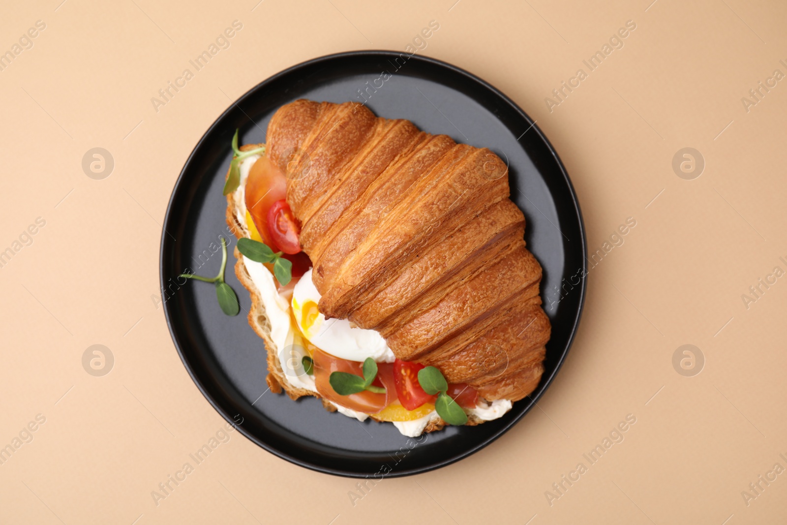 Photo of Tasty croissant with fried egg, tomato and microgreens on beige background, top view