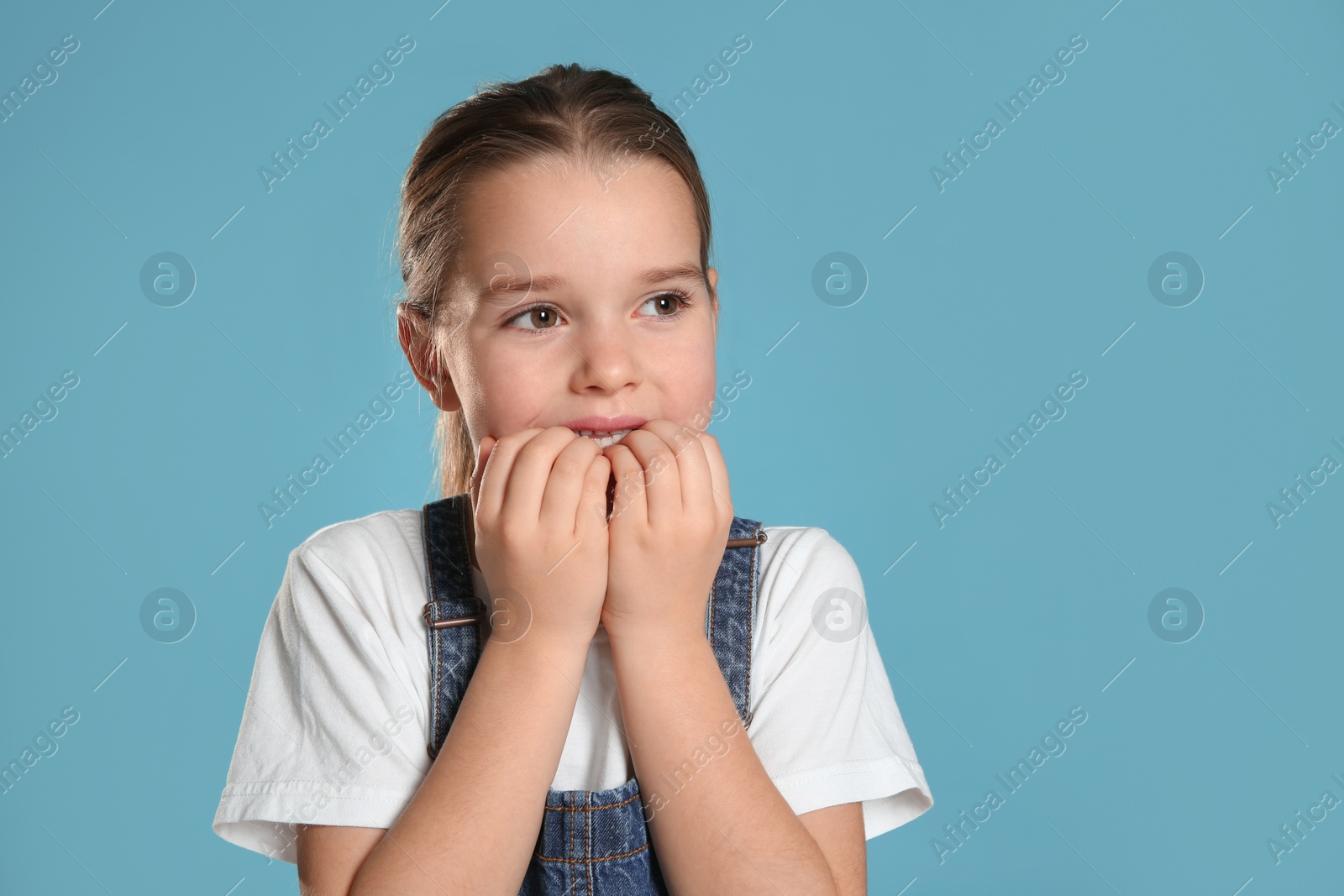 Photo of Cute little girl biting her nails on turquoise background. Space for text