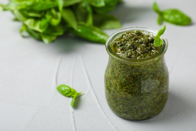 Photo of Jar with basil pesto sauce on table. Space for text