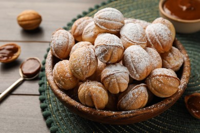 Bowl of delicious nut shaped cookies with boiled condensed milk on wooden table, closeup