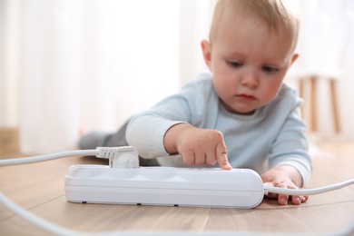 Photo of Little child playing with power strip on floor indoors, selective focus. Dangerous situation