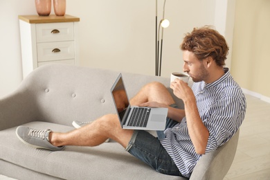 Young man with laptop sitting on sofa at home