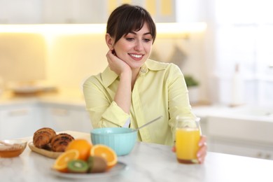 Photo of Smiling woman with glass of juice having breakfast at home