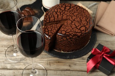 Photo of Delicious chocolate truffle cake, red wine and gift box on wooden table