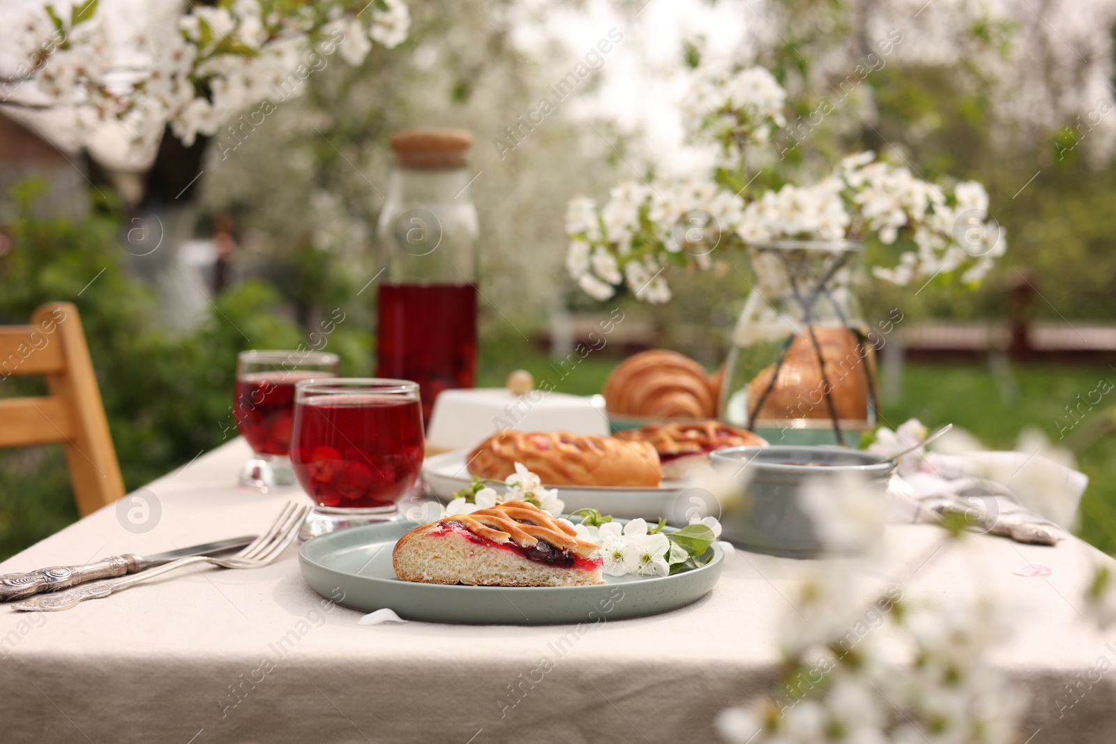 Photo of Stylish table setting with beautiful spring flowers, fruit drink and pie in garden