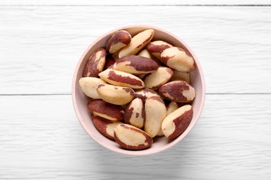 Photo of Bowl of delicious Brazil nuts on white wooden table, top view