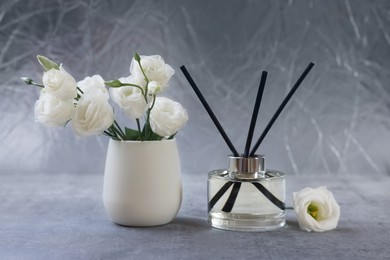 Reed diffuser and vase with eustoma flowers on gray marble table