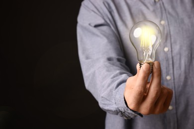 Photo of Glow up your ideas. Closeup view of man holding light bulb on black background, space for text