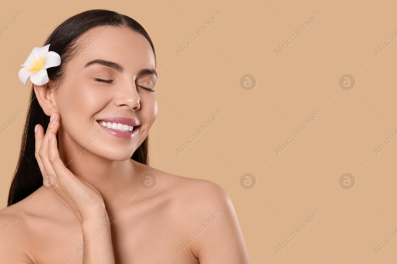 Photo of Young woman with plumeria flower in hair on beige background, space for text. Spa treatment