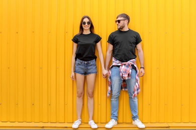 Photo of Young couple wearing black t-shirts near color wall on street